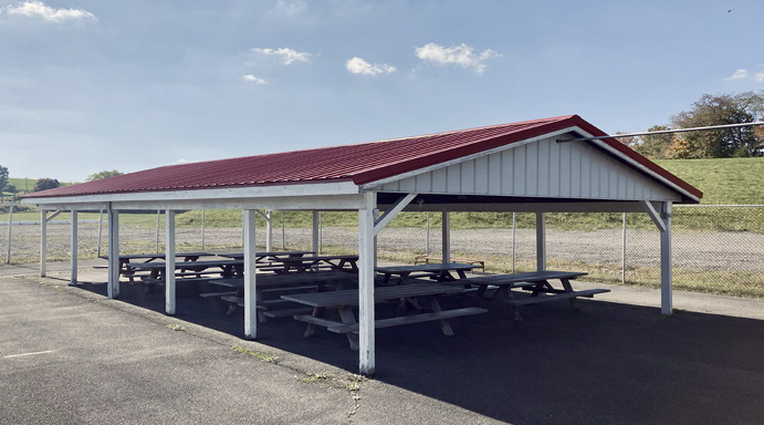 A red-roofed pavilion with picnic tables behind the grandstands